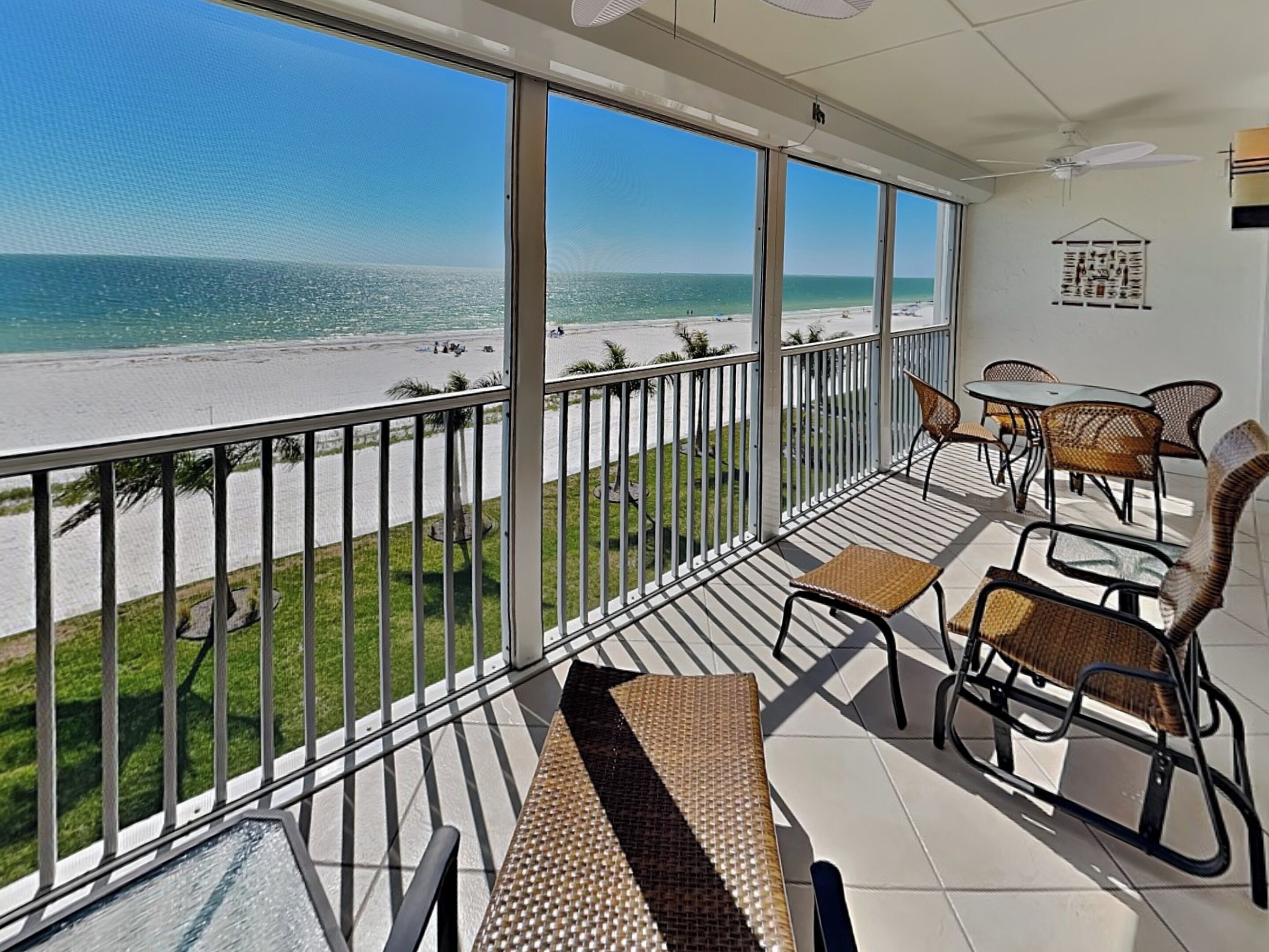 A balcony with a view of the beach, wicker furniture, and a ceiling fan.