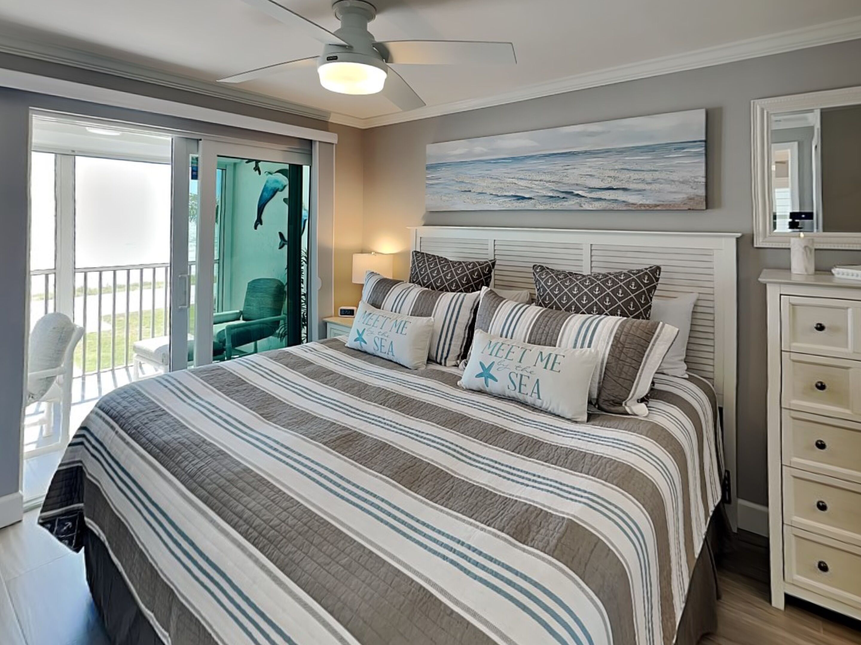 Ein Schlafzimmer mit einem Bett, einem Deckenventilator, einem Gemälde, einem Nachttisch und einem Sessel.