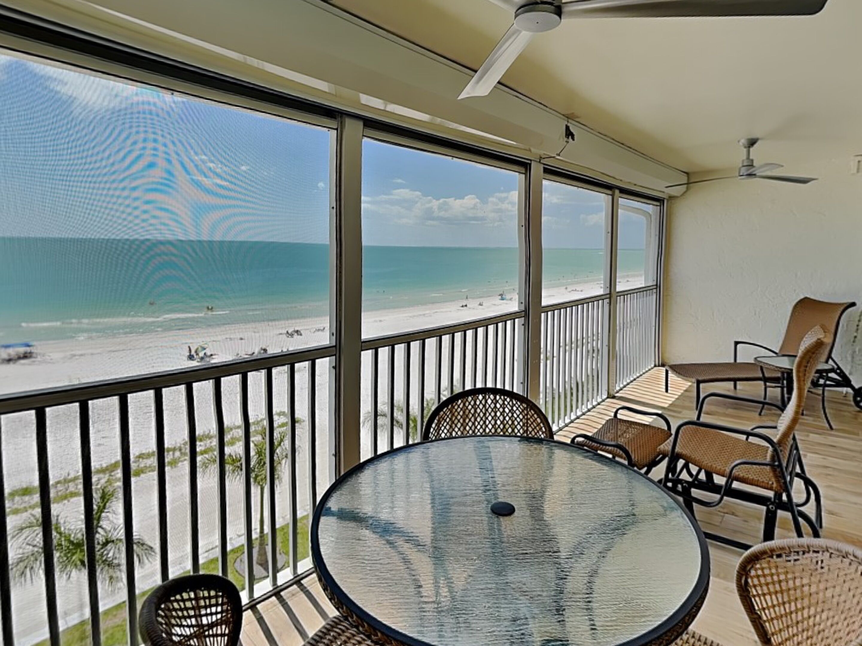 A balcony with a glass table and chairs, overlooking a beach.