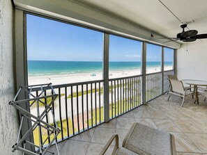 A balcony with a view of a beach, a ceiling fan, and a table with chairs. - Pointe South 201 (Fort Myers Beach)