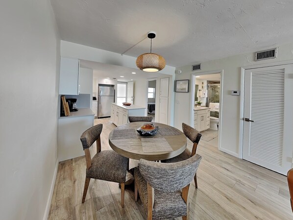 A modern kitchen with white cabinets, a dining area with a round table and chairs, and a hanging light fixture. - Pointe South 201 (Fort Myers Beach)