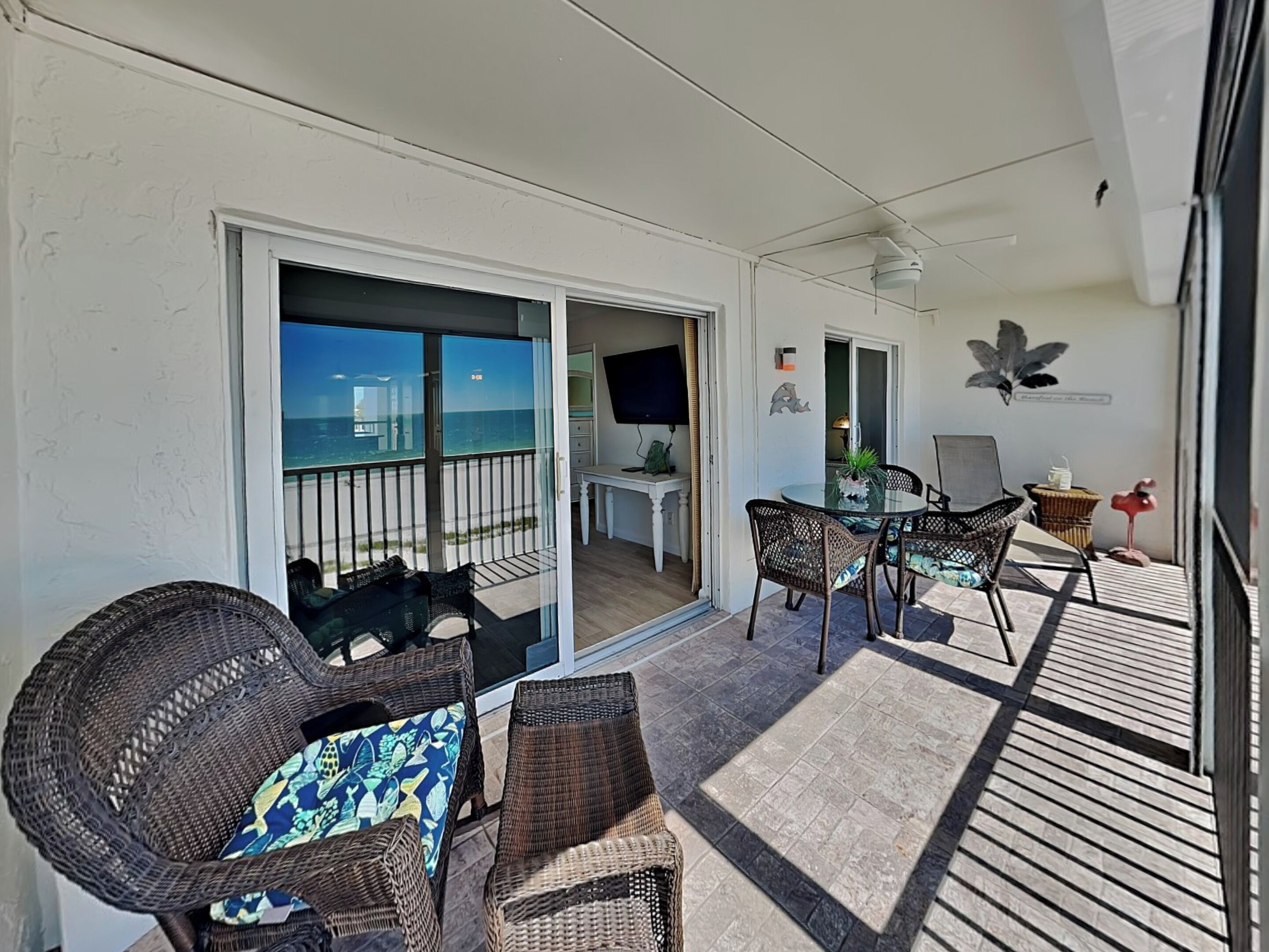 A balcony with wicker furniture, a dining table, and chairs, overlooking the ocean.