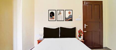 A hotel room with a bed, a nightstand, a lamp, a door, and three framed pictures on the wall.