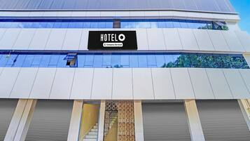 A modern hotel building with a prominent 'HOTEL' sign, a company-serviced logo, and a staircase leading to the entrance.