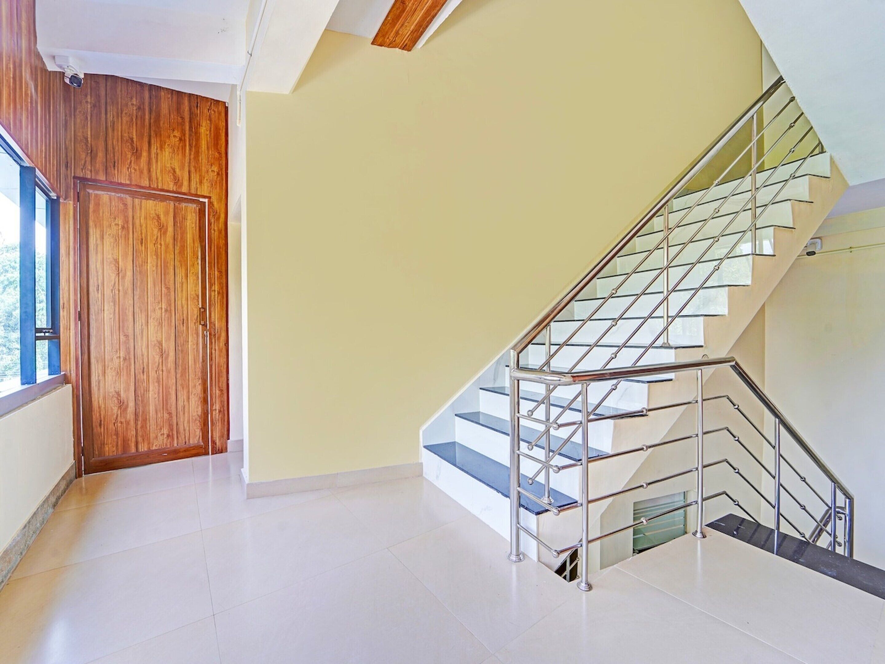 Un interior moderno con una puerta de madera, una escalera con barandillas de vidrio y una pared lisa.