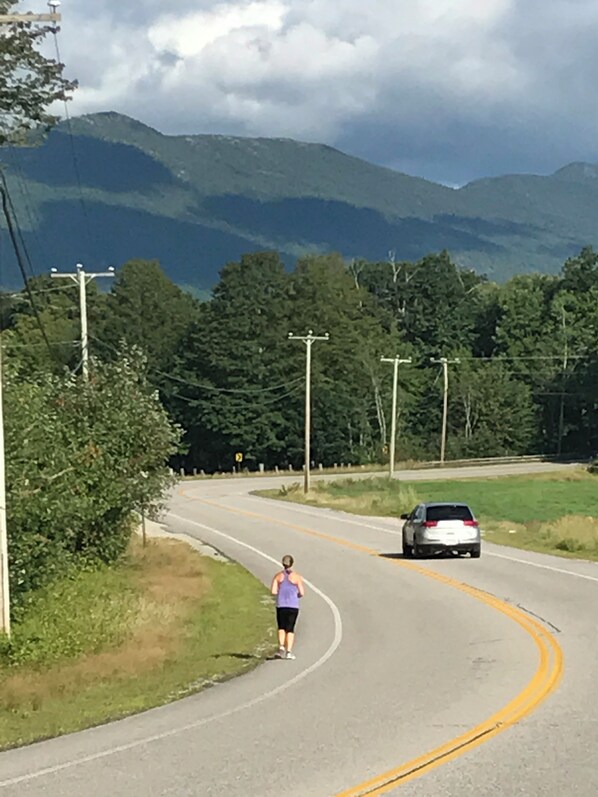 A winding road with a person jogging and a car approaching a curve.