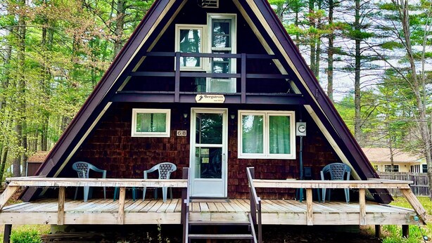 Una cabaña triangular con un porche, una puerta y dos ventanas.