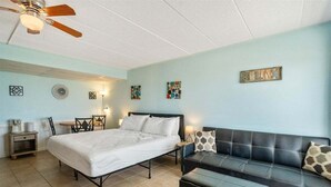 Un dormitorio con cama, un sofá de cuero negro, una mesita y un ventilador de techo.