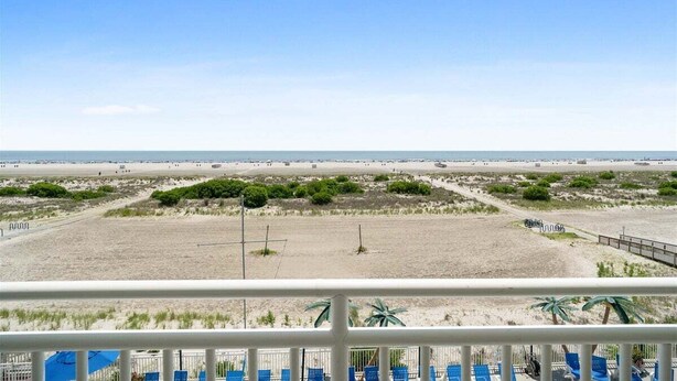 Vista a la playa desde un balcón con barandilla, una playa arenosa y vegetación escasa.