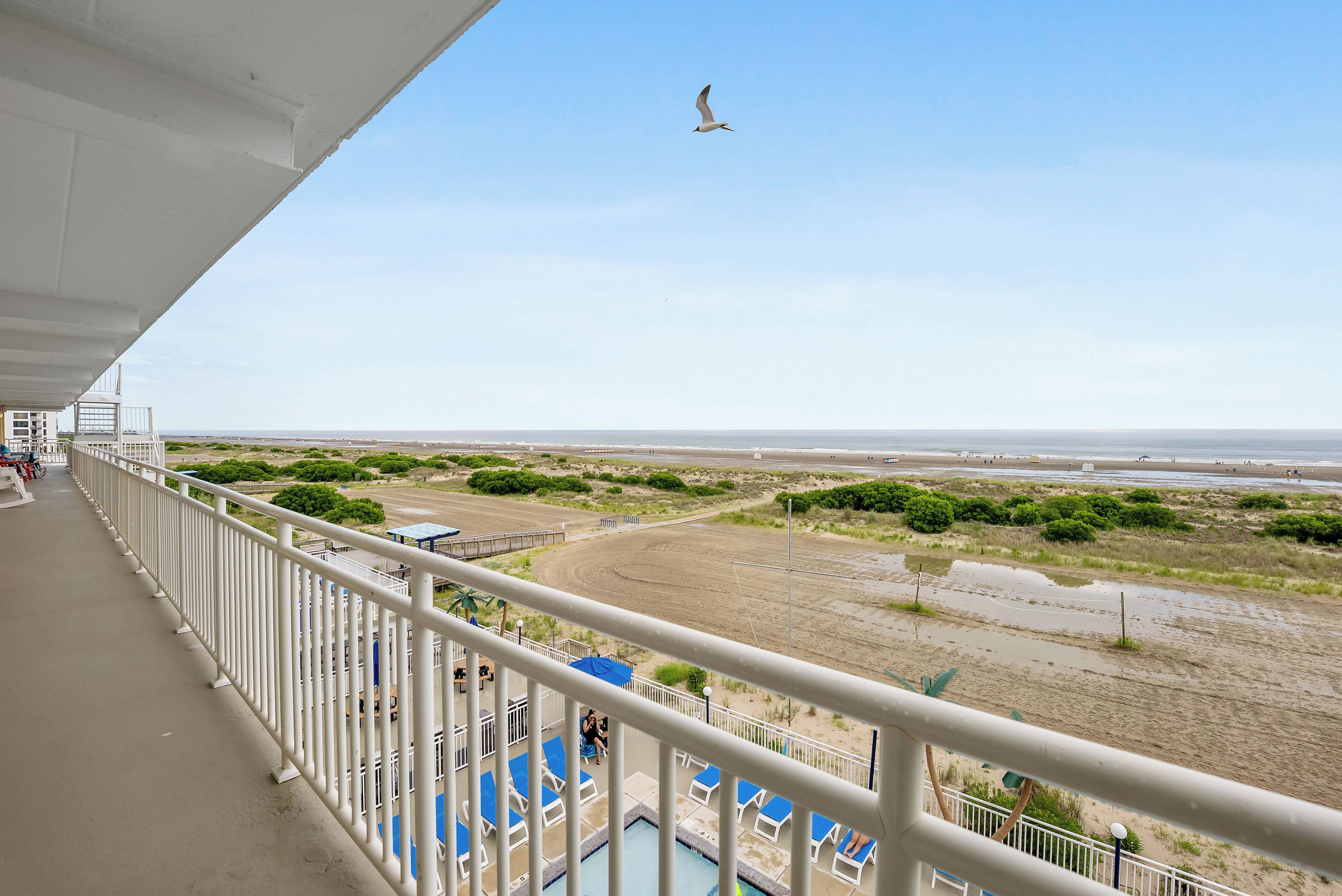 A balcony with a view of a beach and a pool area.