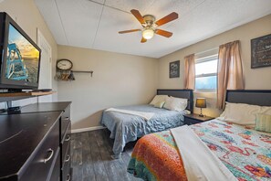 A bedroom with two beds, a ceiling fan, a clock, and a TV on a dresser. - 1 Bedroom Beach Condo with a Pool & Balcony (Wildwood Crest)