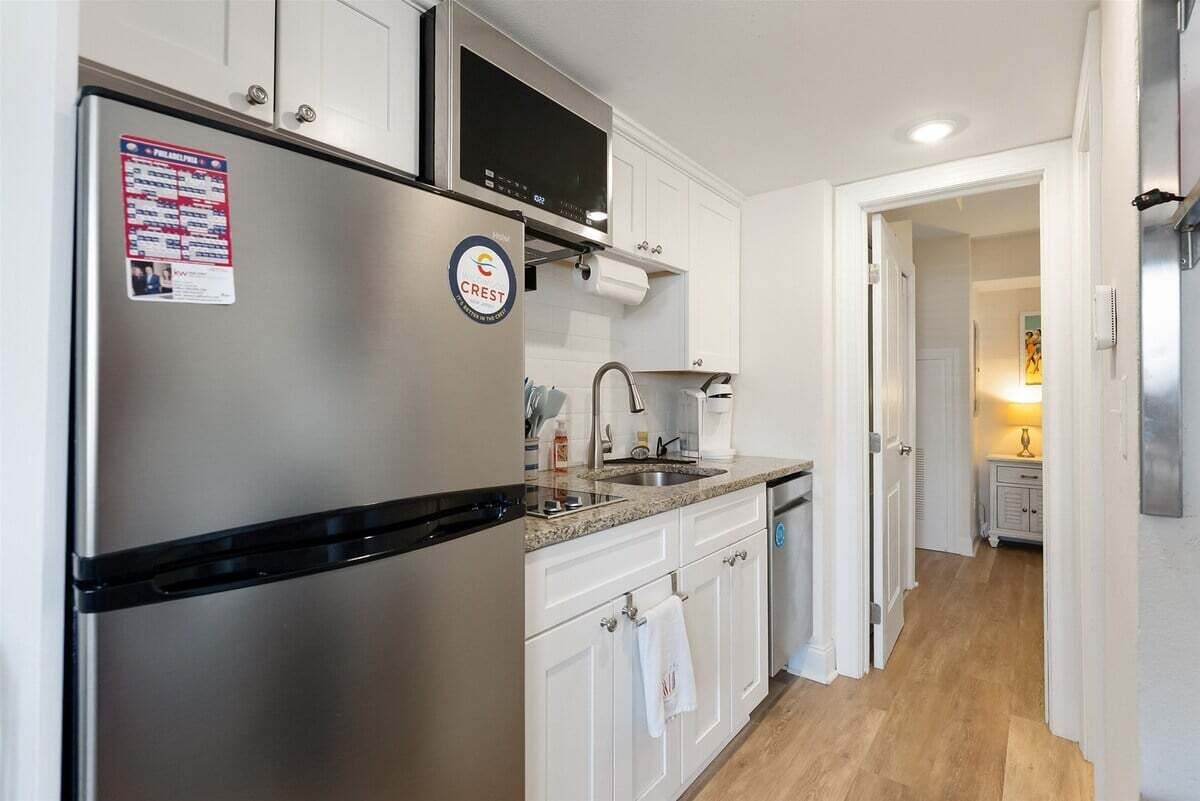 A modern kitchen with stainless steel appliances, white cabinetry, and a granite countertop.