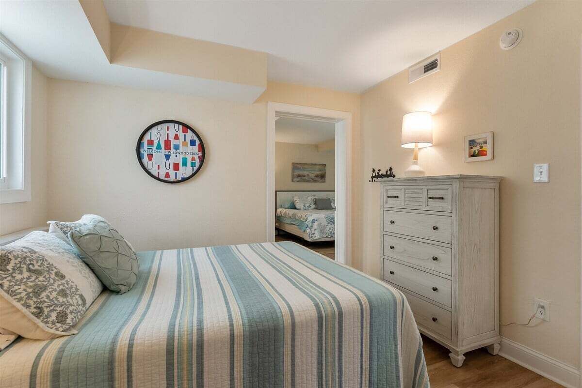 A bedroom with a bed, a dresser, a wall clock, and a door leading to another room.