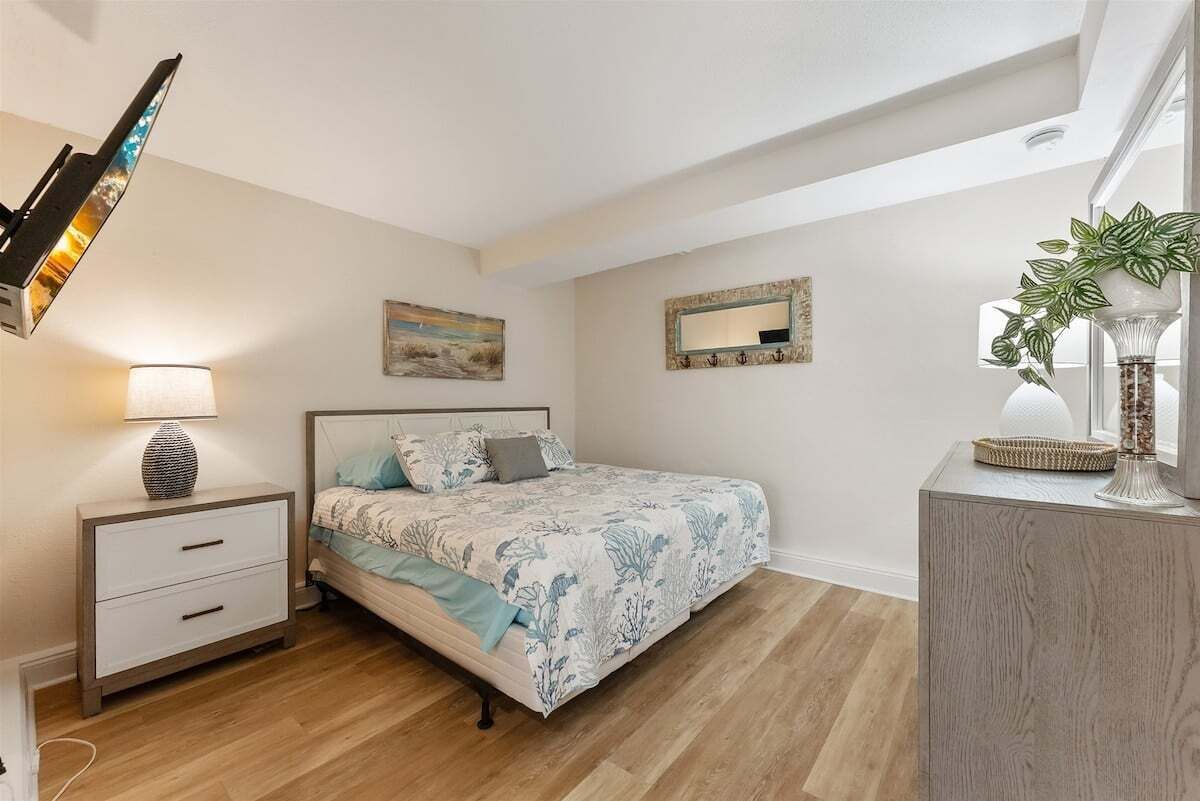 Un dormitorio con cama, mesita de noche, lámpara, decoración en la pared, espejo y una planta en maceta.