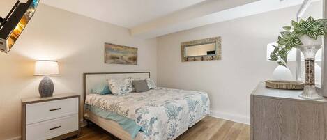 Un dormitorio con cama, mesita de noche, lámpara, decoración en la pared, espejo y una planta en maceta.