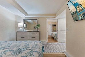 Un dormitorio con cama, cómoda, espejo y puerta que da a otra habitación.