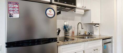 Une cuisine moderne dotée d’appareils électroménagers en acier inoxydable, de meubles blancs et d’un four à micro-ondes placé au-dessus de la cuisinière.