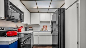 A modern kitchen with white cabinets, a black refrigerator, and a red pot on the stove.