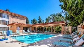 A swimming pool with lounge chairs, a covered area, and a building with a tiled roof.