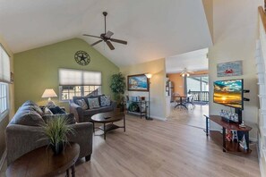 A spacious living room with a ceiling fan, a large window, a television, and a dining area with a table and chairs. - Gorgeous 4 Bedroom Townhome in Diamond Beach (Wildwood Crest)