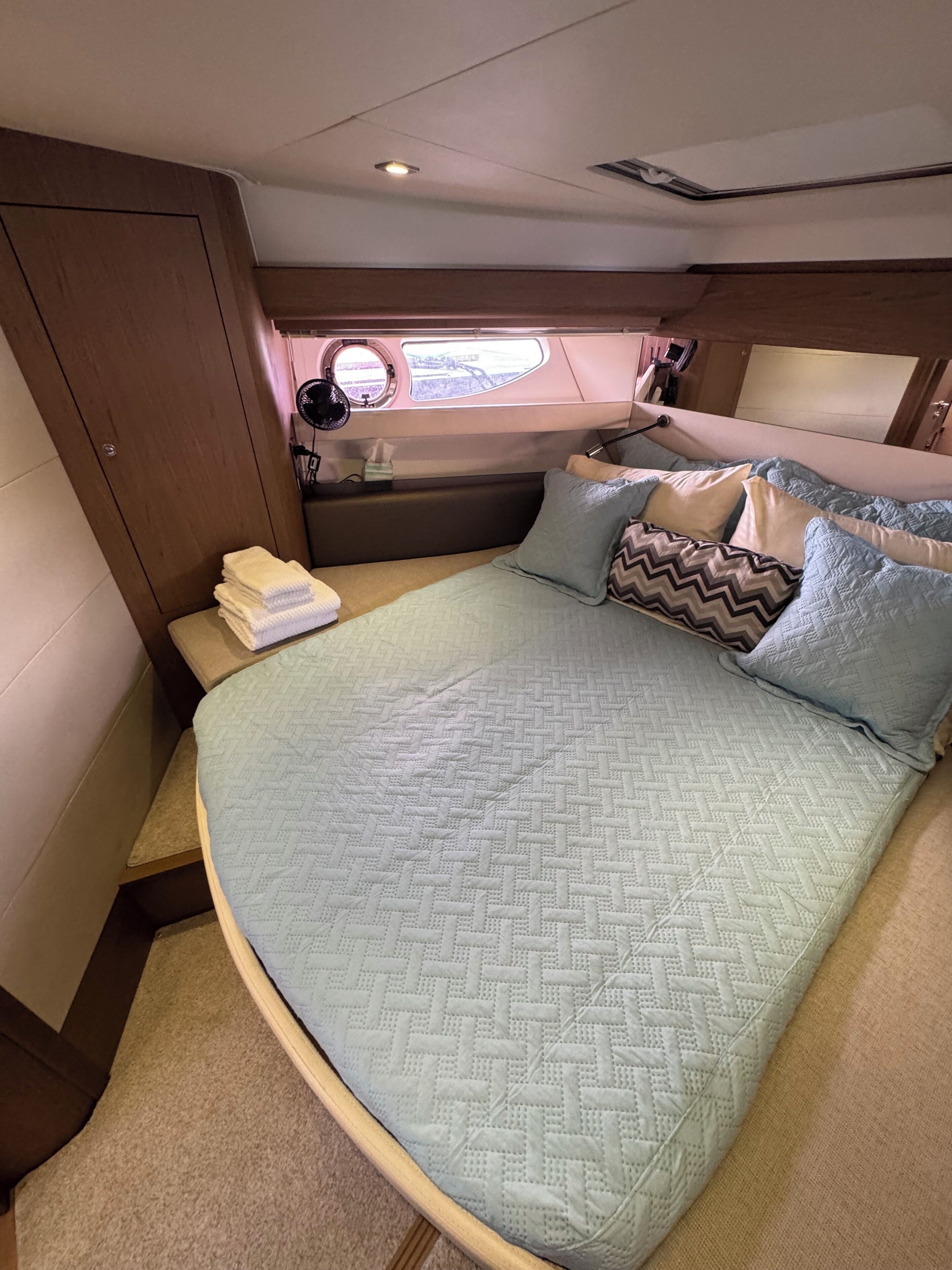 A boat cabin with a bed, a window, and a small table with a lamp.