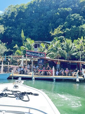 A docked boat with a sign reading 'HOLD IN THE WAY' and a restaurant with outdoor seating.