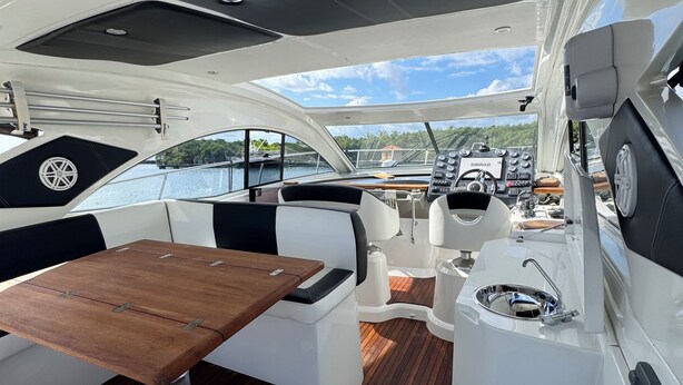 Interior de barco con una mesa de madera, asientos acolchados, un timón y un panel de control.