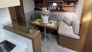 Una cocina compacta con encimera de vidrio, un lavamanos pequeño y una zona de comedor con mesa y banco.