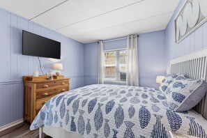 Un dormitorio con cama, cómoda, televisor y ventana con cortinas.