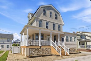A two-story house with a porch, a stone foundation, and a staircase leading to the entrance.