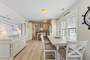 Une cuisine avec des meubles blancs, une table à manger avec des chaises et une grande fenêtre avec des stores.