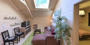 A cozy cabin with a loft bed, a television, a sofa, and a large plant. - Luxury Chalet With Sauna in the Forest (Durbuy)