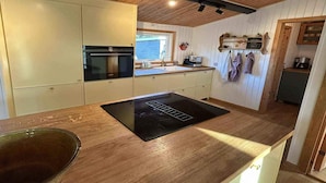 Una cocina con armarios de madera, horno empotrado, cocina por inducción negra y ventana con vistas.