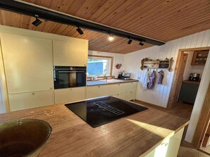 A kitchen with wooden cabinets, a built-in oven, a black induction cooktop, and a window with a view. - 4 Star Holiday Home in Vaeggerlose (Vaeggerlose)