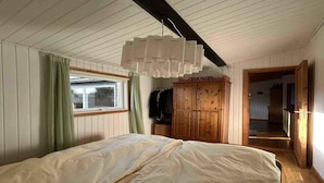 Un dormitorio con cama, un armario de madera, una ventana con cortinas y un pasillo.