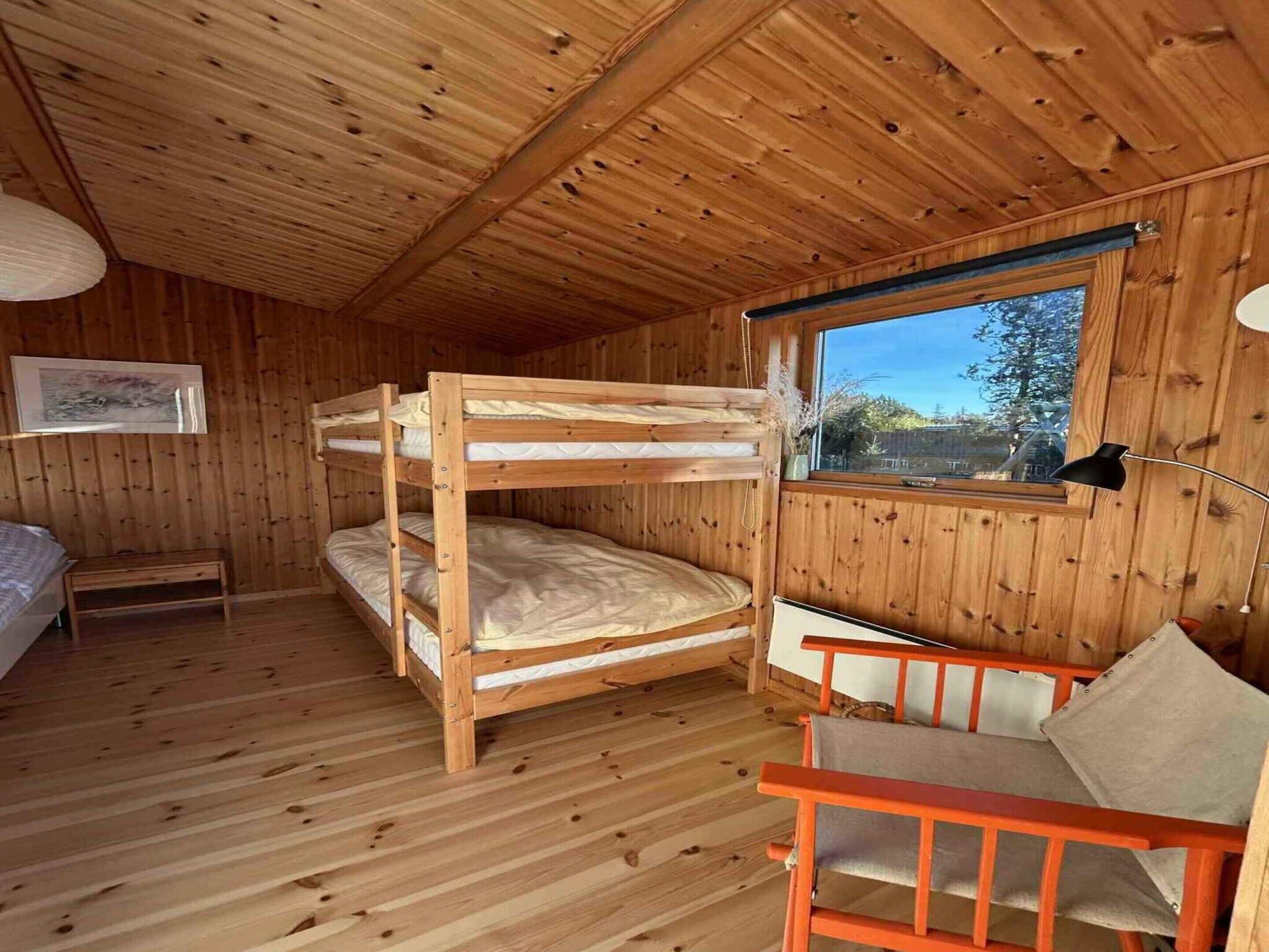 Une chambre dans un chalet en bois, avec des lits superposés, un bureau et une fenêtre.