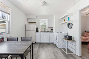 Cozinha compacta com armários brancos, uma mesa de jantar e um balcão pequeno com uma torradeira.