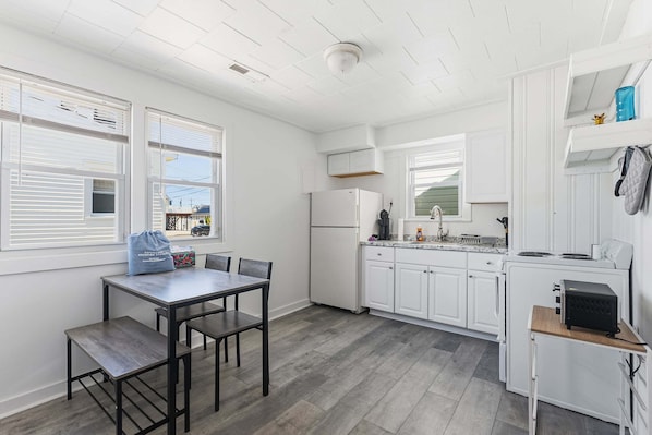 A modern kitchen with white cabinets, a dining table with chairs, a refrigerator, a microwave, and a coffee maker.