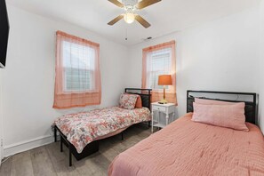 A bedroom with two beds, a ceiling fan, and a bedside table with a lamp.