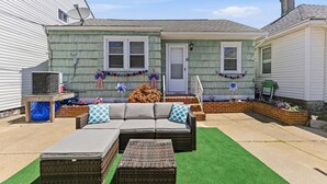 Une terrasse avec un canapé, deux poufs et un barbecue.