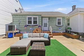A patio with a sofa, two ottomans, and a grill.
