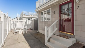 A residential building with a red door, white railings, and a small porch with a table and chairs. - 2BR Steps from Wildwood Beach with Private Outdoor Dining and Shower (Wildwood Crest)