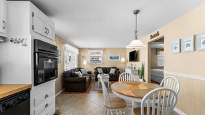 A modern kitchen with a built-in oven and refrigerator, a dining area with a wooden table and white chairs, and a living area with two sofas and a coffee table. - 2BR Steps from Wildwood Beach with Private Outdoor Dining and Shower (Wildwood Crest)