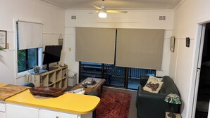 A living room with a yellow table, a black leather sofa, a red rug, and a ceiling fan.