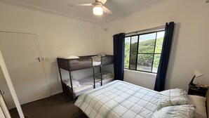A room with bunk beds, a bed with a quilt, a window with curtains, a ceiling fan, and a door.