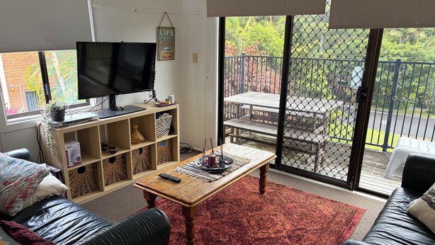 A living room with a TV, shelves, a coffee table, and a view of a patio with outdoor furniture.