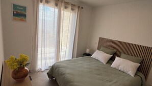 Un dormitorio con cama, mesita de noche, lámpara, ventana con cortinas y una lámpara de pared.