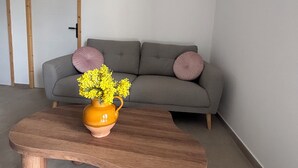 Una sala de estar con un sofá gris, una mesa de centro de madera y un florero con flores amarillas, y un equipo de aire acondicionado en la pared.