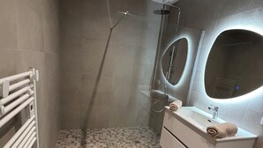 Un baño moderno con ducha, lavamanos con espejo y un perchero para toallas.