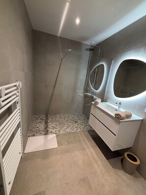 A modern bathroom with a shower, a sink with a mirror, and a towel rack. - Garden apartment between sea and mountains (Arbellara)